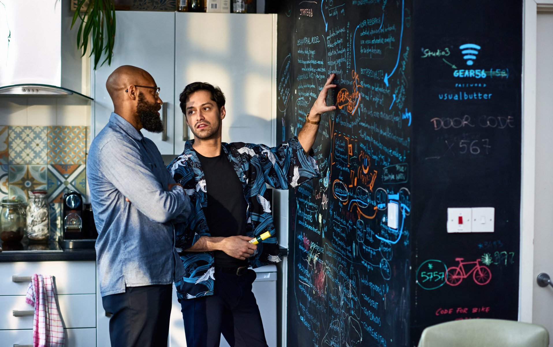 Two men using large creative blackboard in office kitchen to discuss business strategy