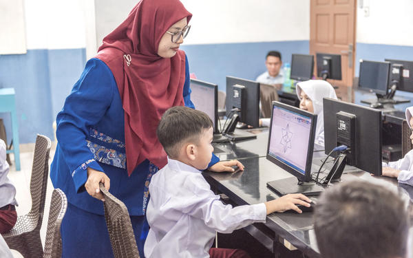 Child and teacher look at computer screen in computer lab