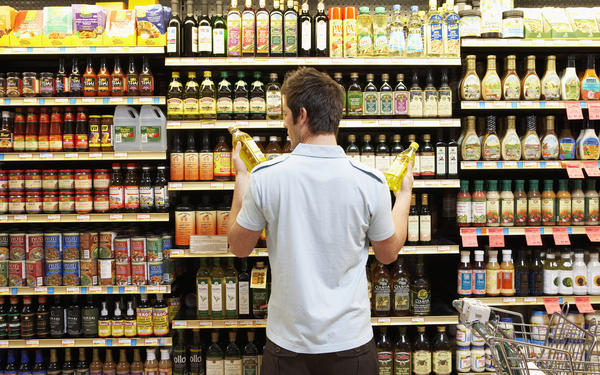 Young man in supermarket comparing bottles of oil