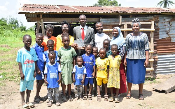 Dedicated Teacher Award Winner Akeem Badru posing for photograph with his award, standing next to colleagues and school children