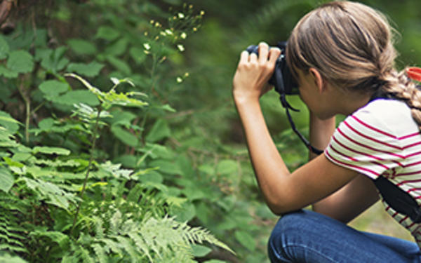 student crouching down in a woodland inspecting the undergrowth through binoculars