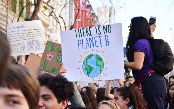 Group of people marching outdoors. One sign reads 'There is no planet B'